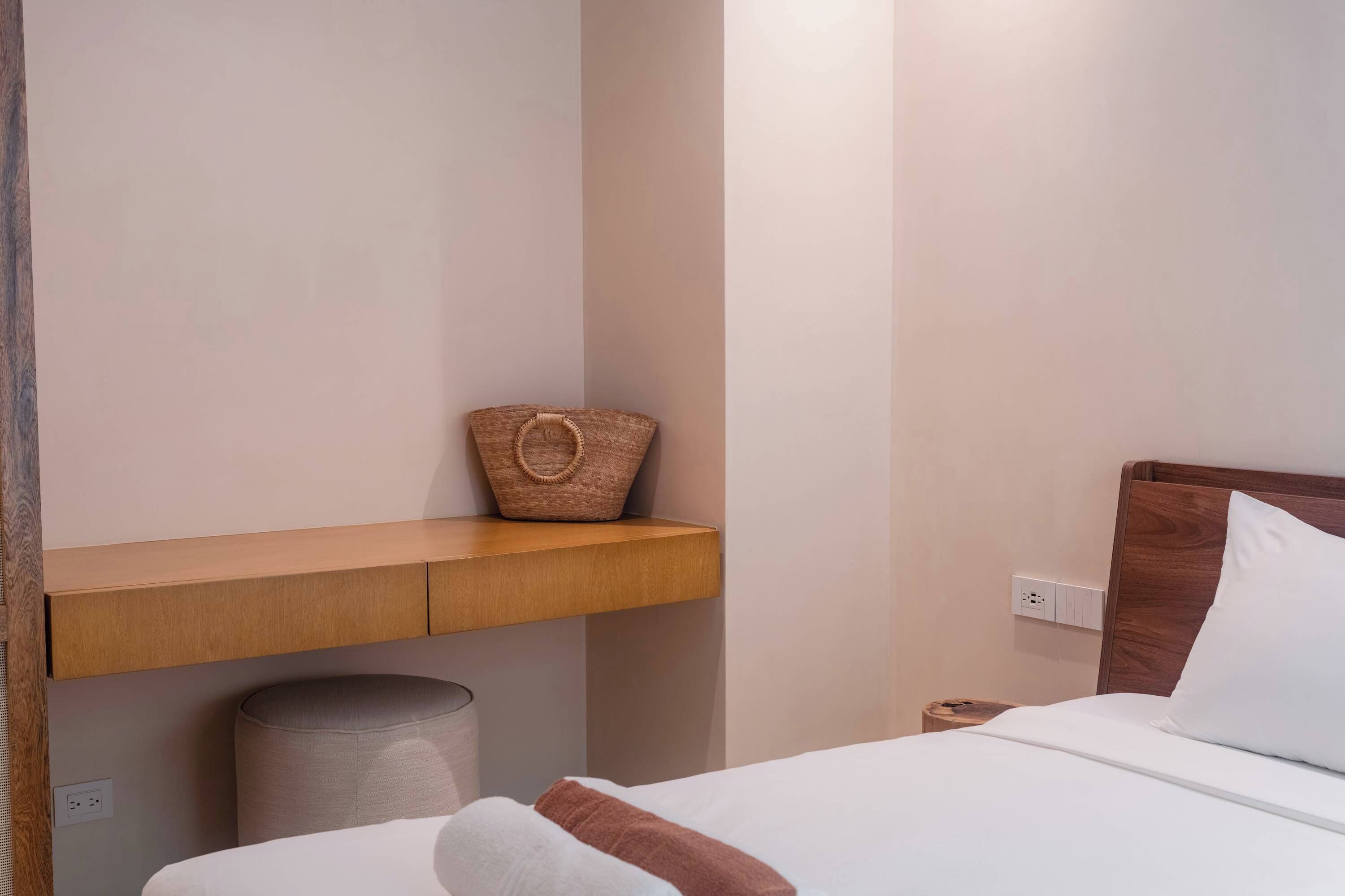 A neatly made bed with a wooden headboard, a bedside table with a woven basket, and a wall socket.