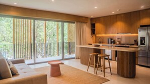 A modern kitchen with a central island, bar stools, and a large window overlooking greenery. - Luxury 1BR Aflora Retreat in Aldea Zama with  pool (Tulum)