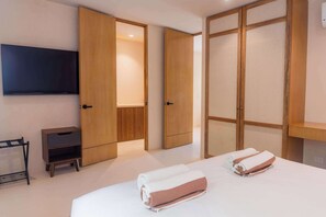 Habitació d'hotel amb un llit, dues tovelloles, un televisor, una taula petita i portes de fusta.