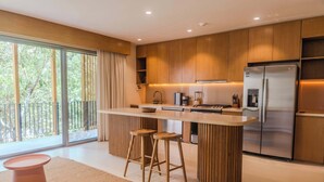 A modern kitchen with a central island, bar stools, a refrigerator, and a view of the outdoors. - Luxury 1BR Aflora Retreat in Aldea Zama with  pool (Tulum)