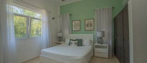 A bedroom with a bed, two bedside tables, a ceiling fan, a window with curtains, and a wardrobe.