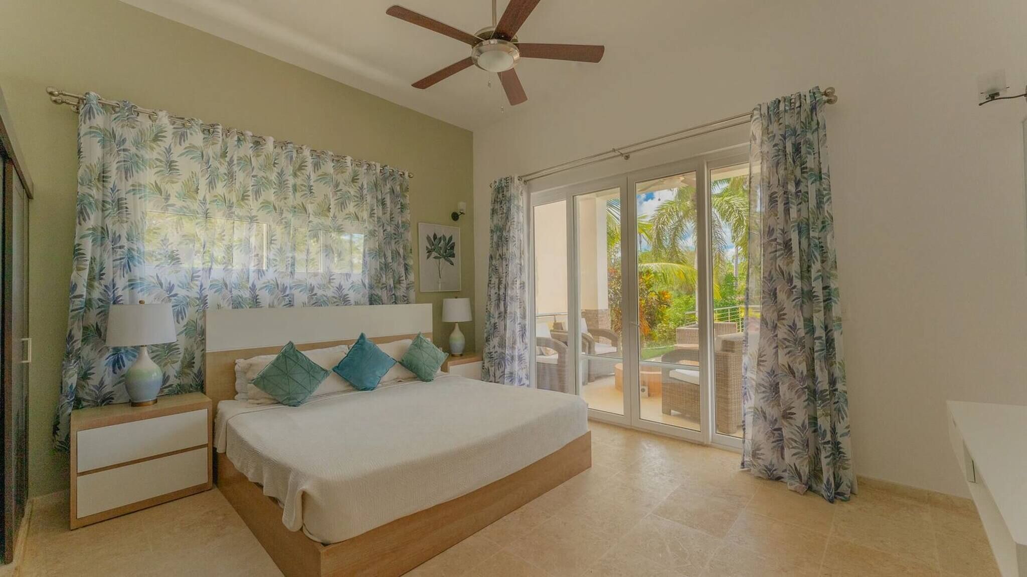 A bedroom with a bed, nightstands, a ceiling fan, and a view of the outdoors through a sliding glass door.