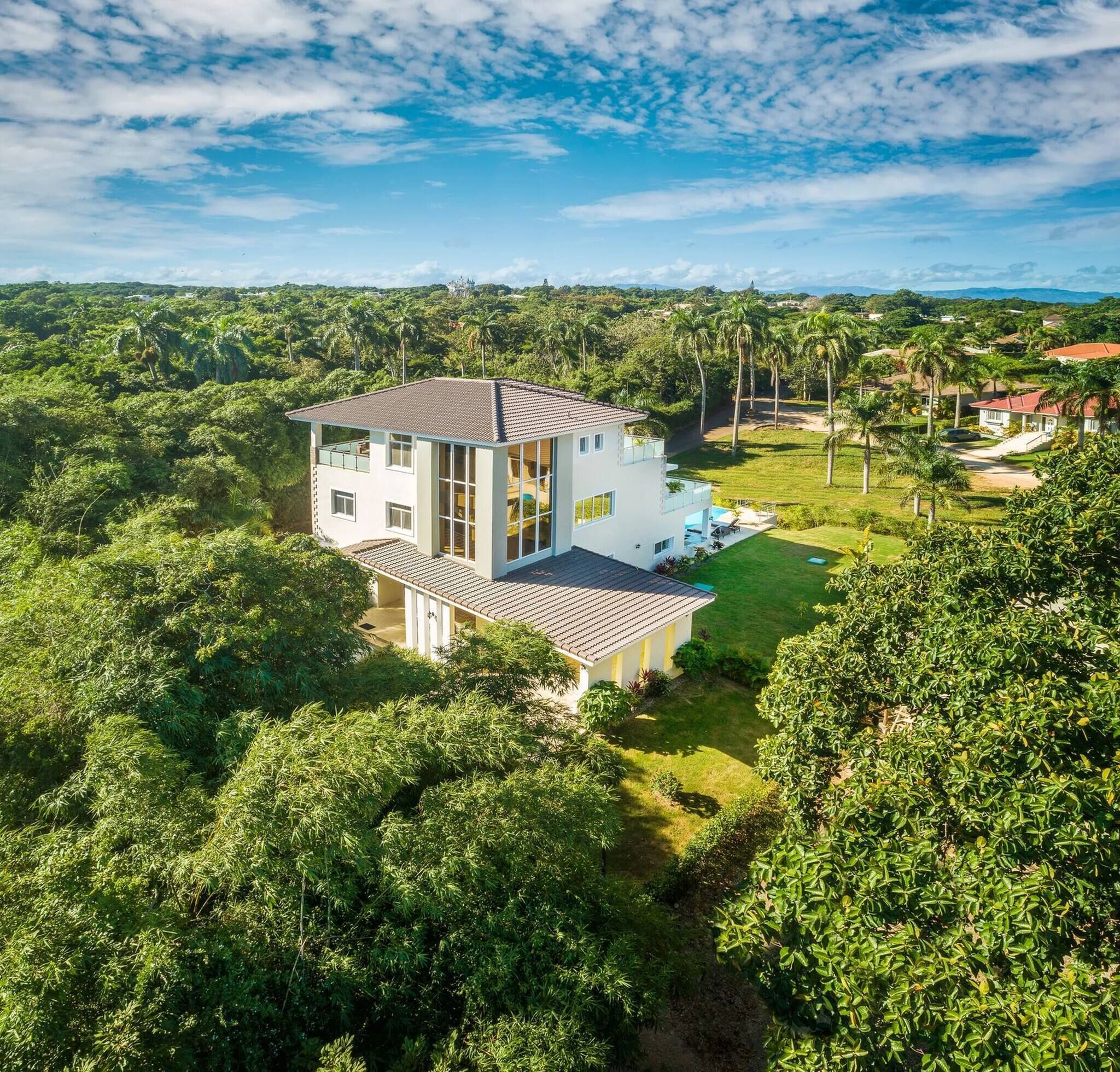 A two-story house with a balcony, surrounded by lush greenery and a clear sky.