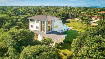 A two-story house with a balcony, surrounded by lush greenery and a clear sky.