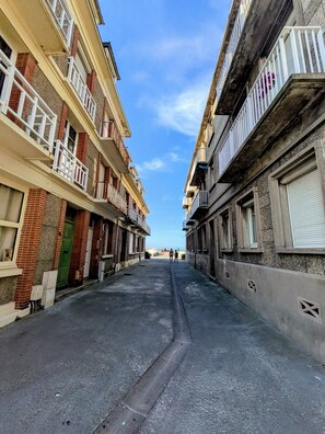 A narrow street flanked by multi-story buildings with balconies, a clear sky, and a distant view of the sea. - right by the sea (Saint-Valery-en-Caux)
