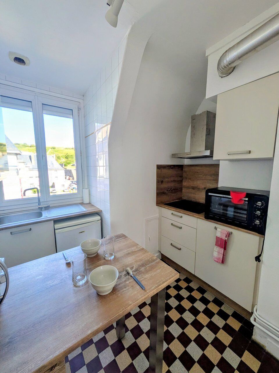 Una cocina compacta con ventana, microondas y piso a cuadros.