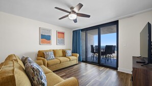 A living room with a sofa, a ceiling fan, and a view through a glass door to an outdoor area. - Lei Lani 104 (Orange Beach)