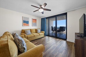 Ein Wohnzimmer mit einer Couch, einem Deckenventilator und Blick durch eine Glastür auf einen Außenbereich.