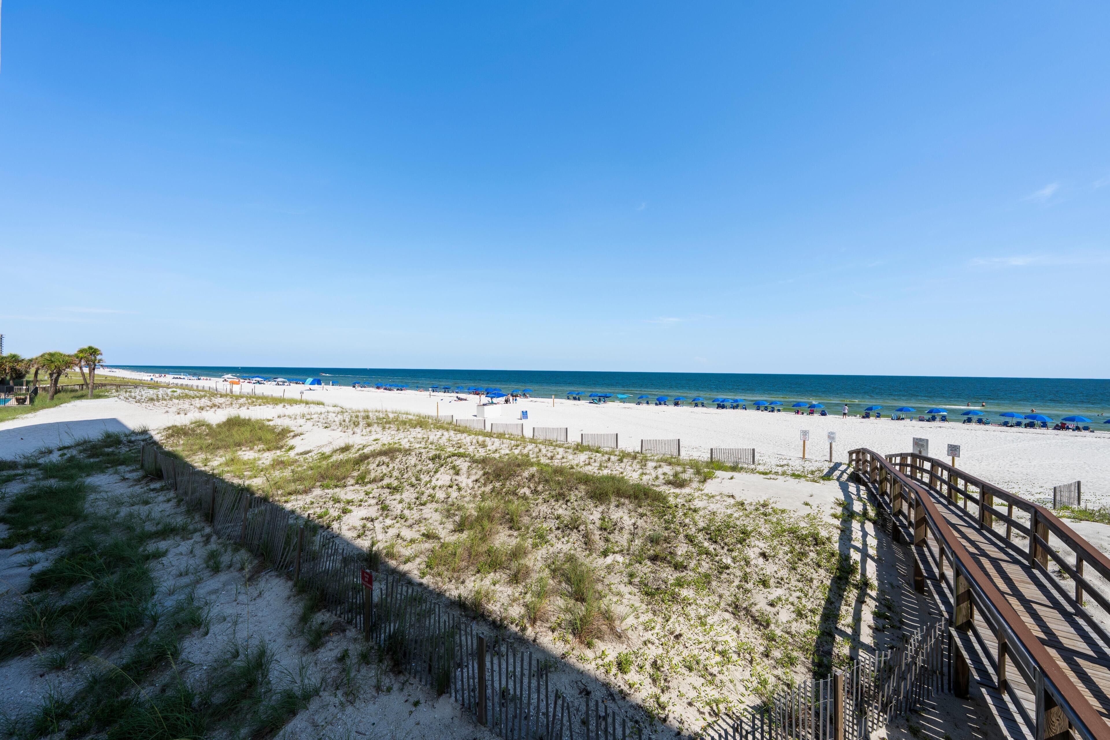 A beach with a wooden boardwalk, sandy dunes, and a clear blue sky.