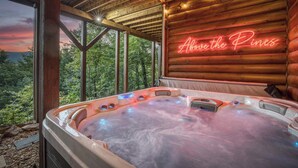 Uma banheira de hidromassagem com um letreiro de neon que diz 'Above the Pines' em um ambiente de cabana de tronco.
