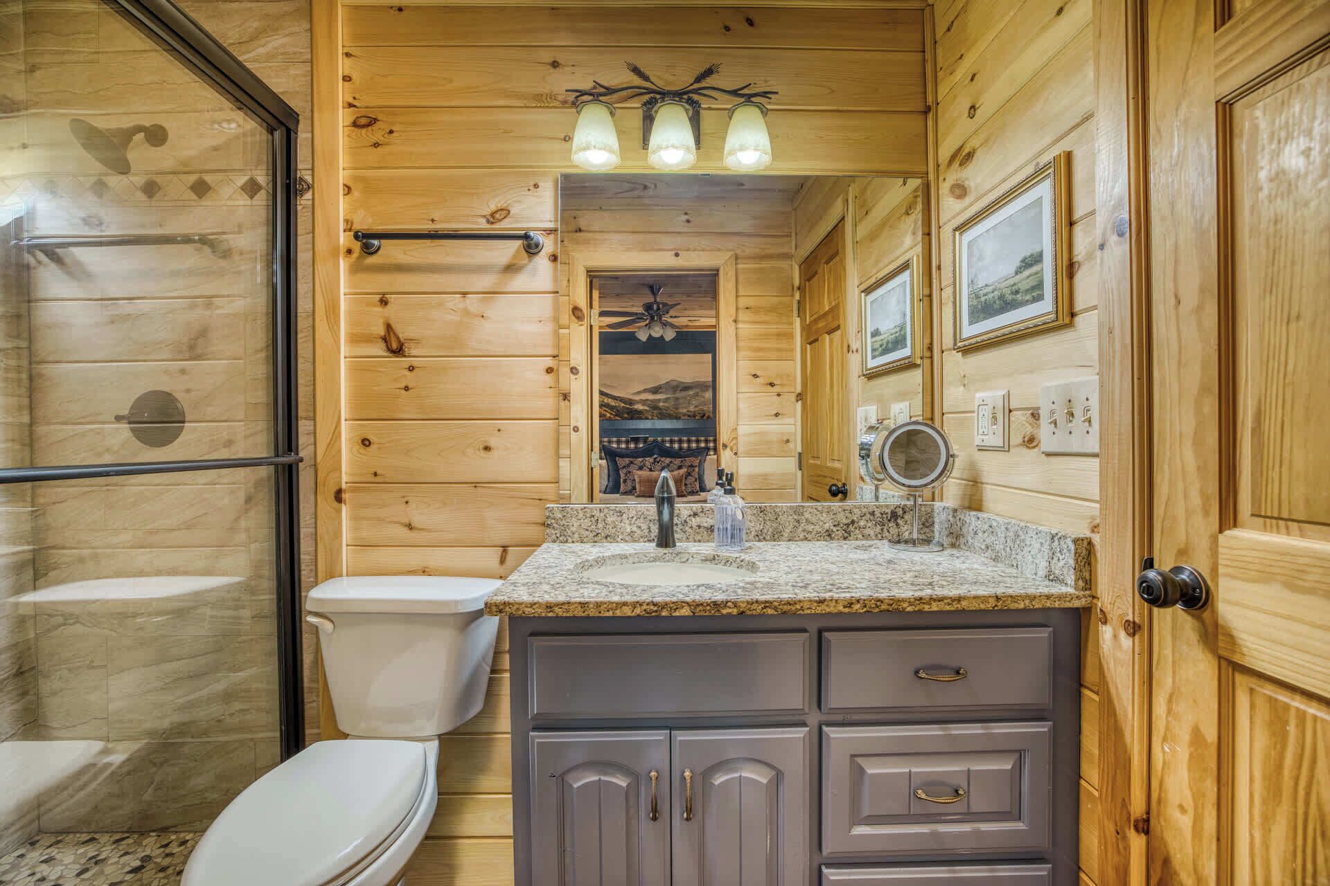 A wooden cabin bathroom with a toilet, sink, vanity, and a ceiling fan.