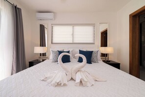 A hotel room with a large bed, two nightstands, a window with blinds, and a mirror. - Luxe Villa in the Caribbean Gated Pool & Sun (Sosúa)