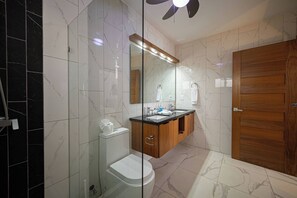 A modern bathroom with a glass shower enclosure, a toilet, a vanity with a sink, and a wooden door. - Luxe Villa in the Caribbean Gated Pool & Sun (Sosúa)