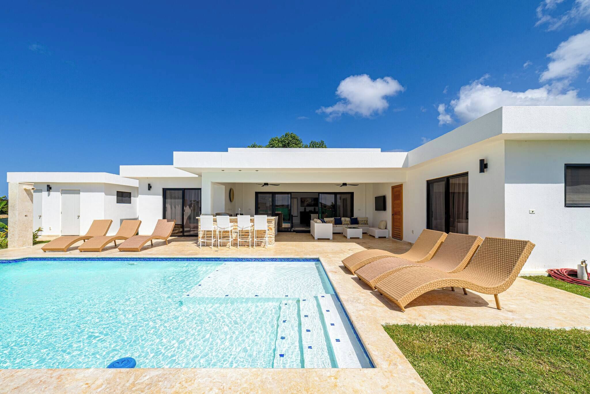 A modern house with a swimming pool, lounge chairs, and a patio area.