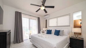 Camera d'albergo moderna con un letto grande, una ventola a soffitto, un comodino, una TV e una porta scorrevole in vetro.