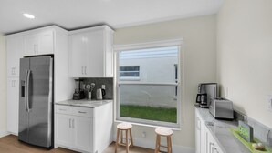 Una cocina moderna con armarios blancos, un refrigerador de acero inoxidable, una cafetera y un ventanal con vistas a un espacio verde.