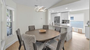 Una cocina moderna con armarios blancos, una isla central y un comedor con mesa redonda y sillas.