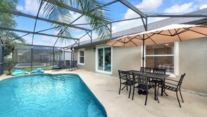 Una piscina con un porche cubierto, mobiliario exterior y vista al jardín.