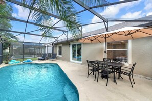 Ein Schwimmbad mit überdachter Terrasse, Gartenmöbeln und Blick auf den Garten.