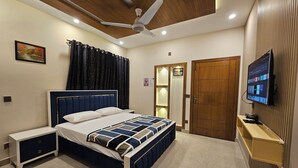 A bedroom with a bed, bedside tables, a ceiling fan, a TV, and a door.