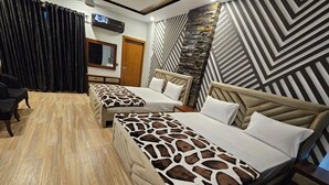 A hotel room with two beds, a wooden floor, a stone accent wall, and a television.
