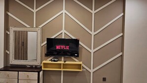 A modern room with a ceiling fan, a flat-screen TV on a wooden shelf, and a mirrored wardrobe.