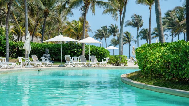 A pool with clear water, surrounded by white lounge chairs and umbrellas, with palm trees in the background. - Depto. Playa & Piscina Acapulco 4 Rec (Acapulco de Juarez)