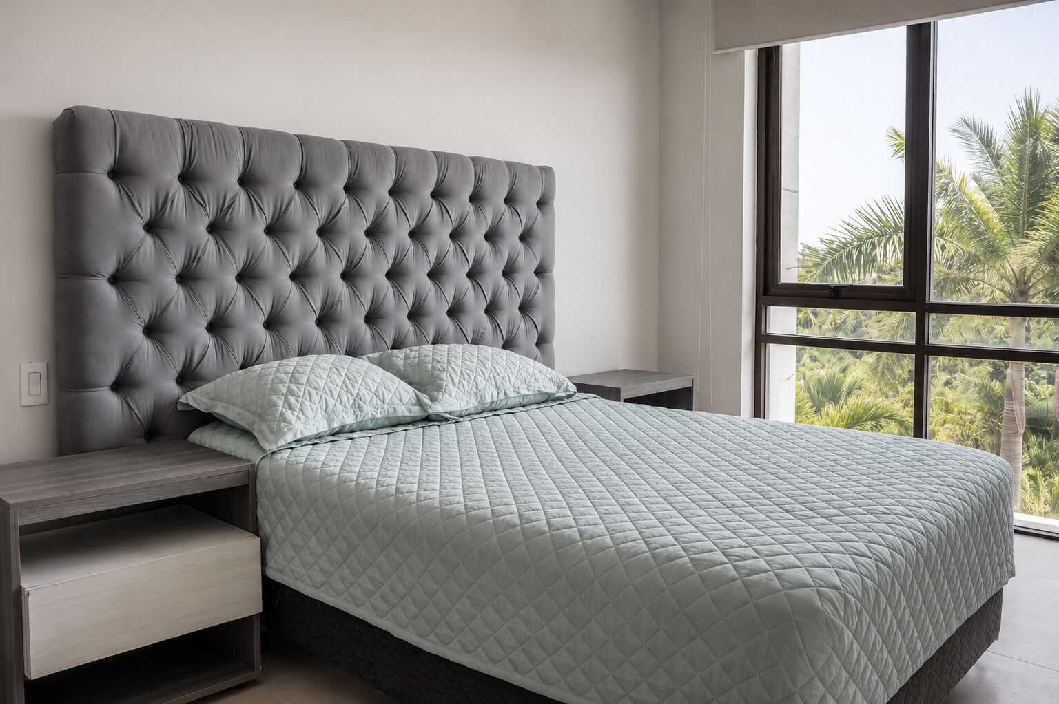 A bedroom with a tufted headboard, a quilted bedspread, and a nightstand.