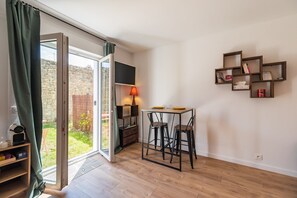 Une pièce comprenant une table, des chaises, une lampe, une bibliothèque et donnant sur l’extérieur.