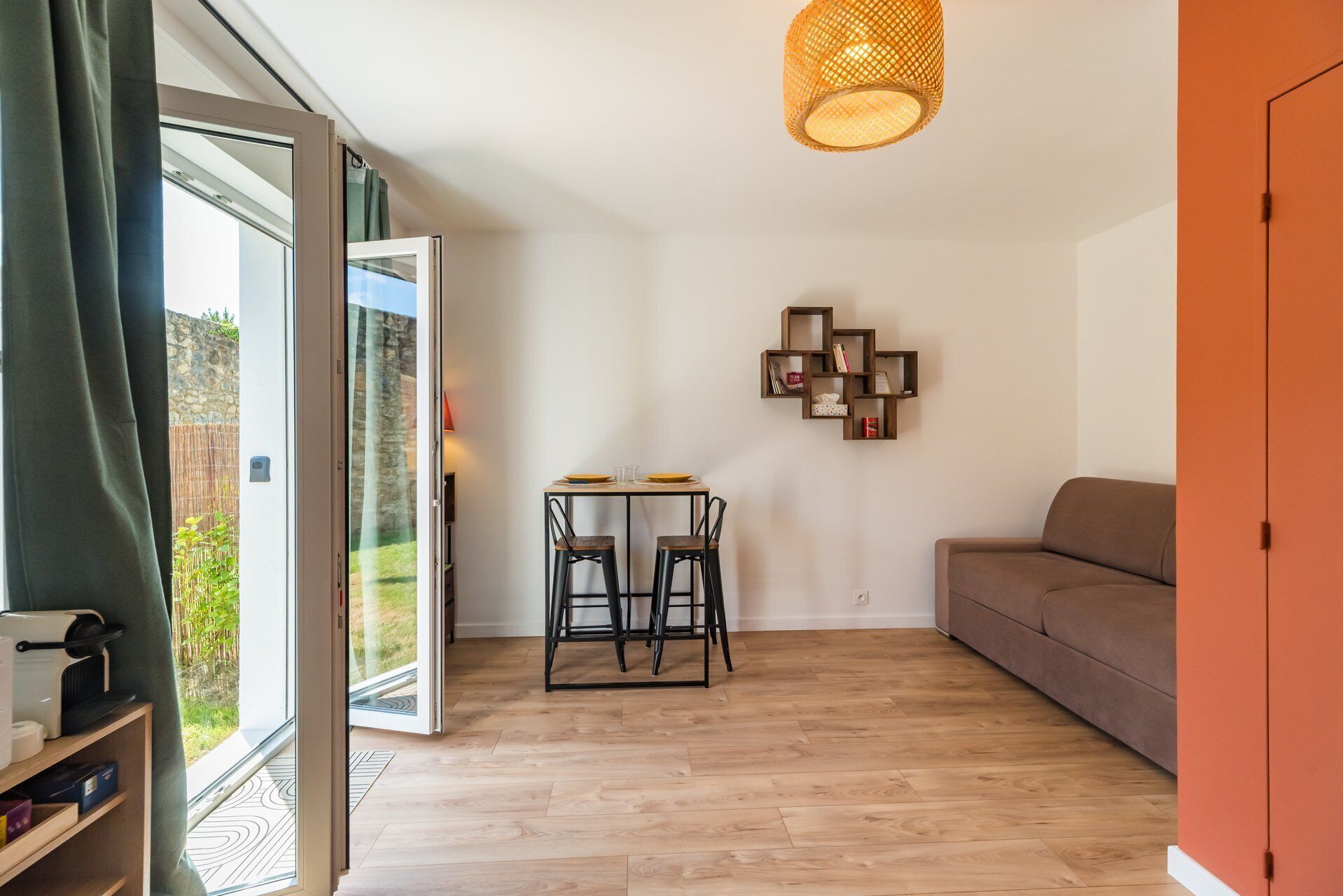 Un salon moderne avec un plancher en bois, un canapé, une table à manger avec des chaises, une étagère murale et une grande fenêtre.