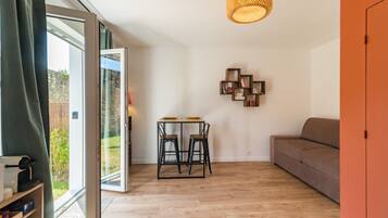 Un salon moderne avec un plancher en bois, un canapé, une table à manger avec des chaises, une étagère murale et une grande fenêtre.
