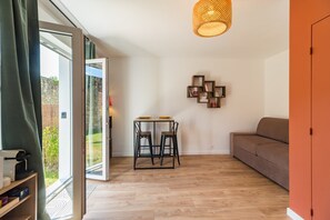 Un salon moderne avec un plancher en bois, un canapé, une table à manger avec des chaises, une étagère murale et une grande fenêtre.