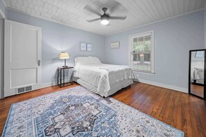 A bedroom with a bed, a standing lamp, a ceiling fan, a window with blinds, and a patterned rug. - Jarrel Cottage Longer Stays Welcome! (Tyler)