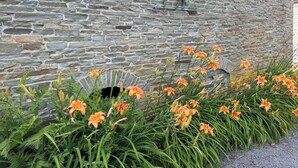 En stenvæg med en ræv skulptur og orange liljer foran.