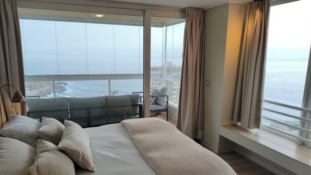 Ein Schlafzimmer mit einem großen Bett, Meerblick und einem Balkon mit Tisch und Stühlen.