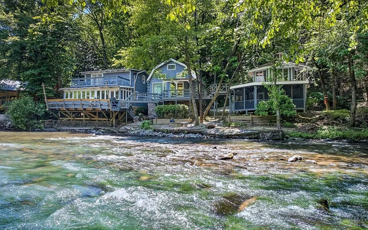 A riverside property with multiple houses connected by bridges, surrounded by dense trees.