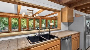 Eine Küche mit Holzschränken, einem Edelstahlkühlschrank und einem großen Fenster mit Blick auf Grünflächen.
