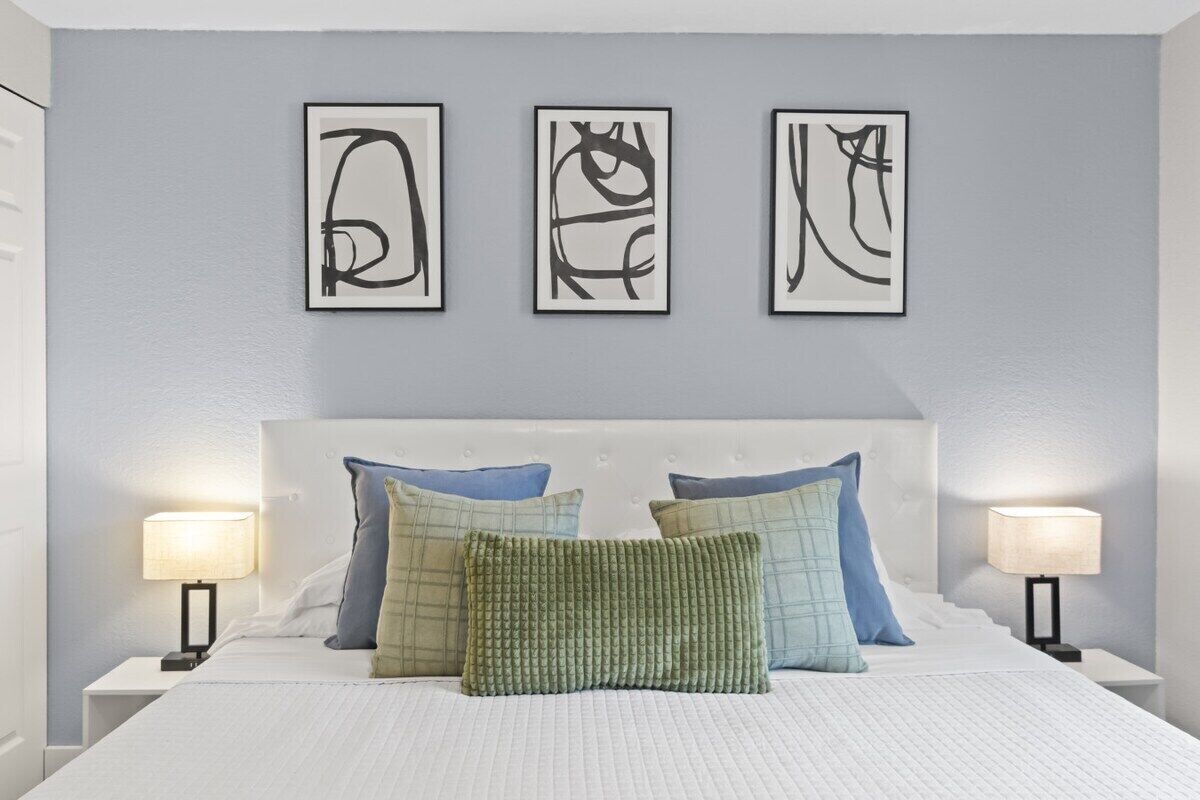 A bedroom with a bed, pillows, bedside tables, and wall art.