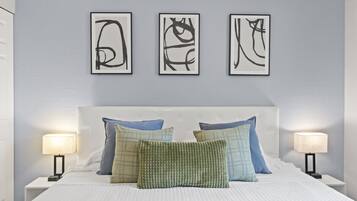 A bedroom with a bed, pillows, bedside tables, and wall art.