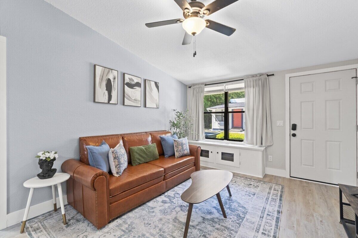 Un salon avec un canapé en cuir marron, une table d’appoint blanche, un tapis à motifs et un ventilateur de plafond.