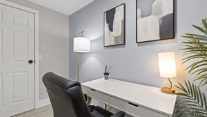 A modern office space with a white desk, black office chair, two wall-mounted lamps, and framed abstract art.