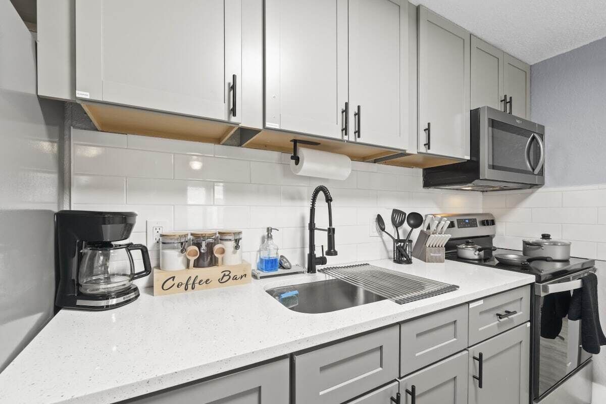 A kitchen with white cabinets, a coffee bar, a sink, a stove, and a microwave.