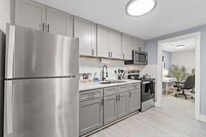 A modern kitchen with stainless steel appliances, grey cabinets, and a microwave.