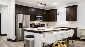 A modern kitchen with dark wood cabinets, stainless steel appliances, a central island with bar stools, and pendant lighting. - Modern Houston Retreat: Free Parking, Group Friendly, Near Med Center & Downtown (Houston)