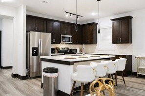 A modern kitchen with dark wood cabinets, stainless steel appliances, a central island with bar stools, and pendant lighting. - Modern Houston Retreat: Free Parking, Group Friendly, Near Med Center & Downtown (Houston)