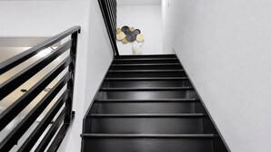 A staircase with black steps and a black railing, leading to a room with a white wall and a decorative wall piece. - Modern Houston Retreat: Free Parking, Group Friendly, Near Med Center & Downtown (Houston)