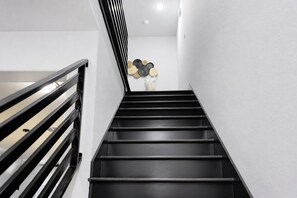 A staircase with black steps and a black railing, leading to a room with a white wall and a decorative wall piece. - Modern Houston Retreat: Free Parking, Group Friendly, Near Med Center & Downtown (Houston)