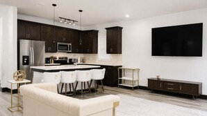 A modern kitchen with dark wood cabinets, a stainless steel refrigerator, a microwave, and a large flat-screen TV mounted on the wall. - Modern Houston Retreat: Free Parking, Group Friendly, Near Med Center & Downtown (Houston)