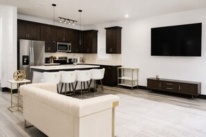 A modern kitchen with dark wood cabinets, a stainless steel refrigerator, a microwave, and a large flat-screen TV mounted on the wall. - Modern Houston Retreat: Free Parking, Group Friendly, Near Med Center & Downtown (Houston)