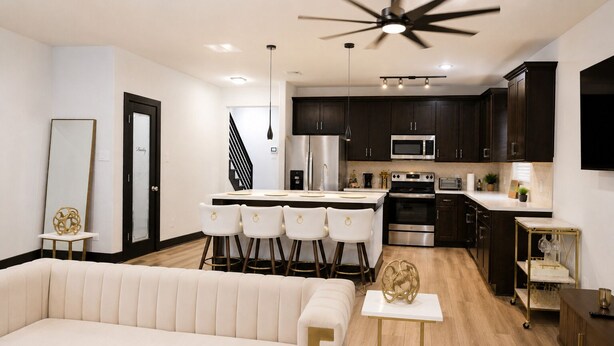 A modern kitchen with dark cabinets, stainless steel appliances, and a central island with bar stools. - Modern Houston Retreat: Free Parking, Group Friendly, Near Med Center & Downtown (Houston)